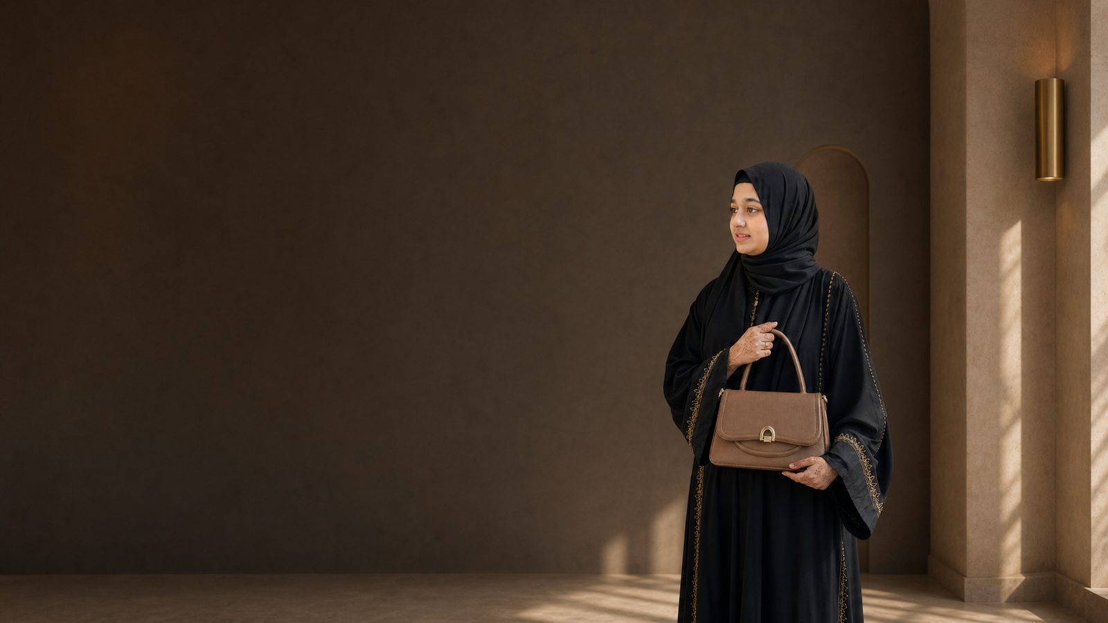 Sanad model in a black abaya carrying a taupe leather handbag